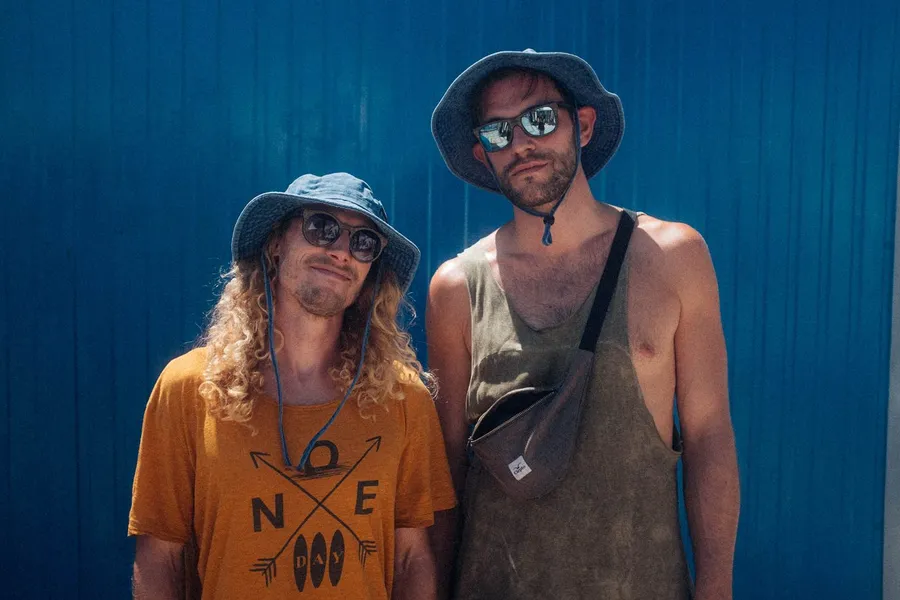 Two men in bucket hats and mirrored sunglasses in front of a blue wall, flash by Kilian Amrehn