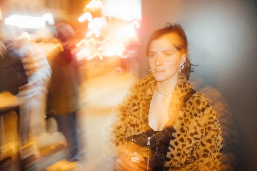 Woman in a leopard coat in a bar, warm light trails from a long exposure, flash by Kilian Amrehn
