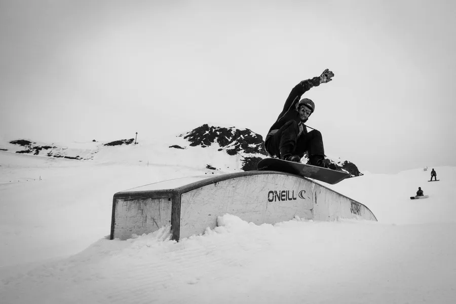 Black and white: snowboarder jumping over a box in a snow park, flash by Kilian Amrehn