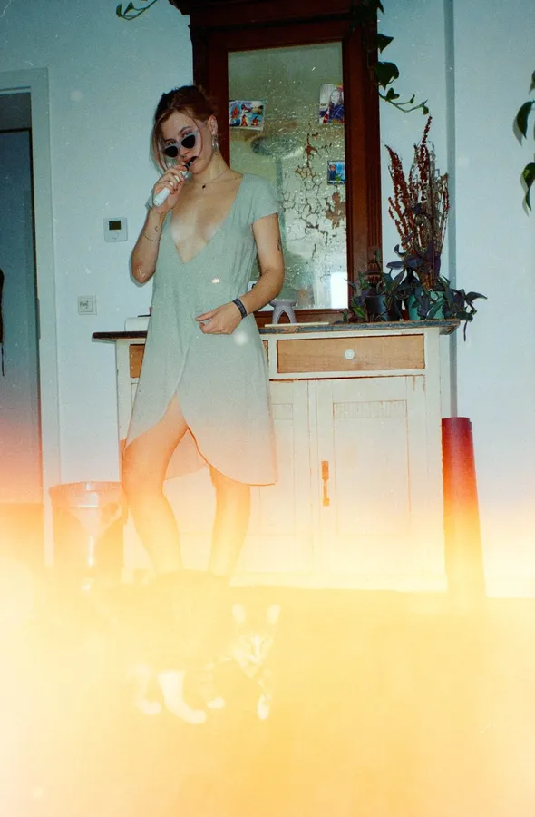 Analogue with light leak: woman in a green dress drinking in a bright room, flash by Kilian Amrehn