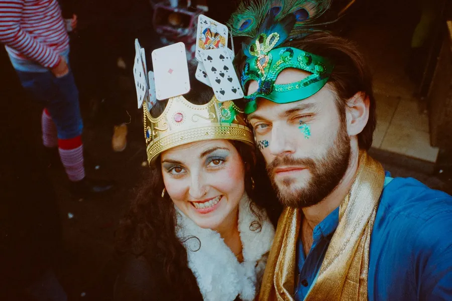Analogue: woman with a playing-card crown and man with a feathered mask, costume party, flash by Kilian Amrehn