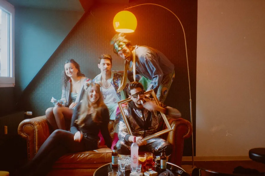 Analogue: friends in glitter outfits on a leather sofa, one holding an empty frame, flash by Kilian Amrehn