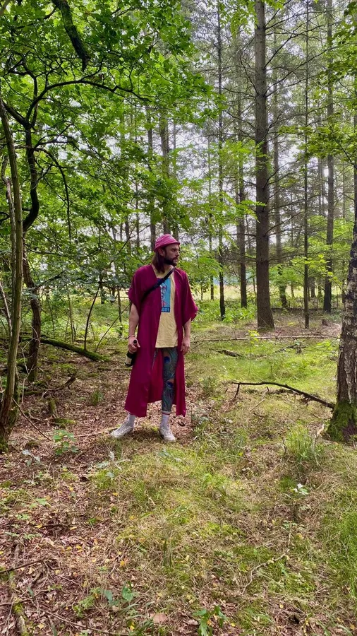 Man in a red coat standing alone in a clearing in a green forest, flash by Kilian Amrehn