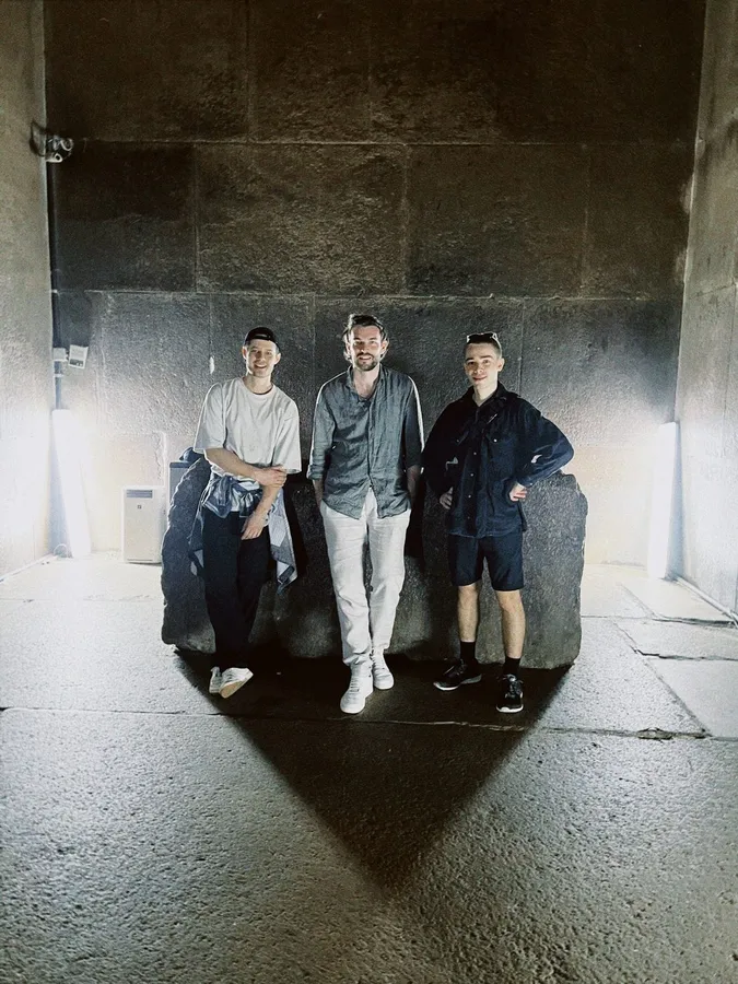 Three men standing in a dark stone burial chamber, hard light, flash by Kilian Amrehn