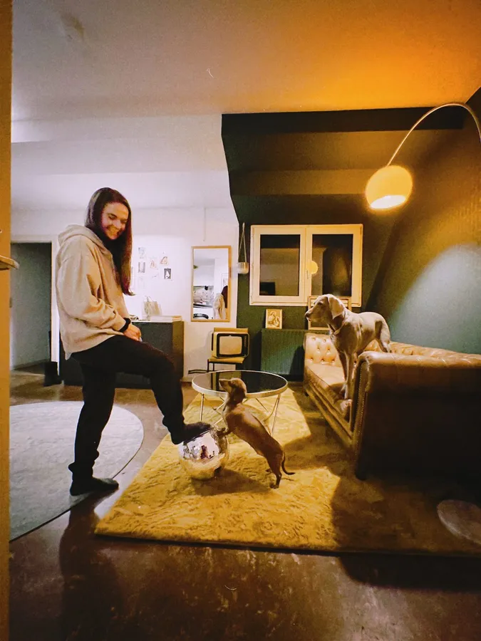 Woman playing with two dogs in a warmly lit living room, flash by Kilian Amrehn