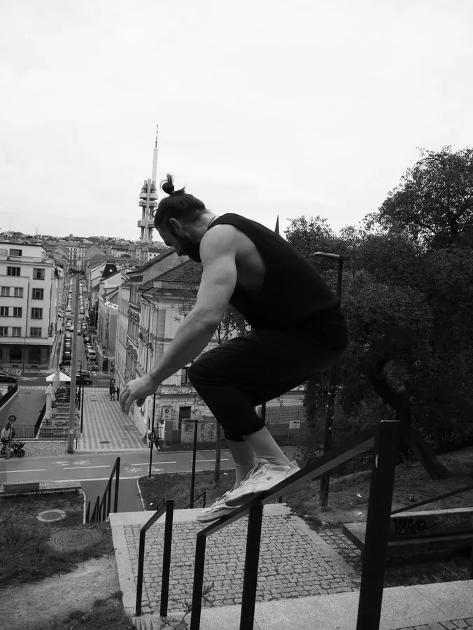 Black and white: man vaulting over a railing, city in the background, flash by Kilian Amrehn