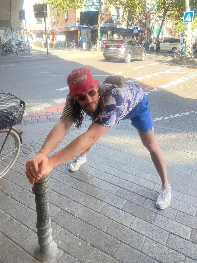 Man in a red cap doing a silly stretch on a bollard on the pavement, flash by Kilian Amrehn