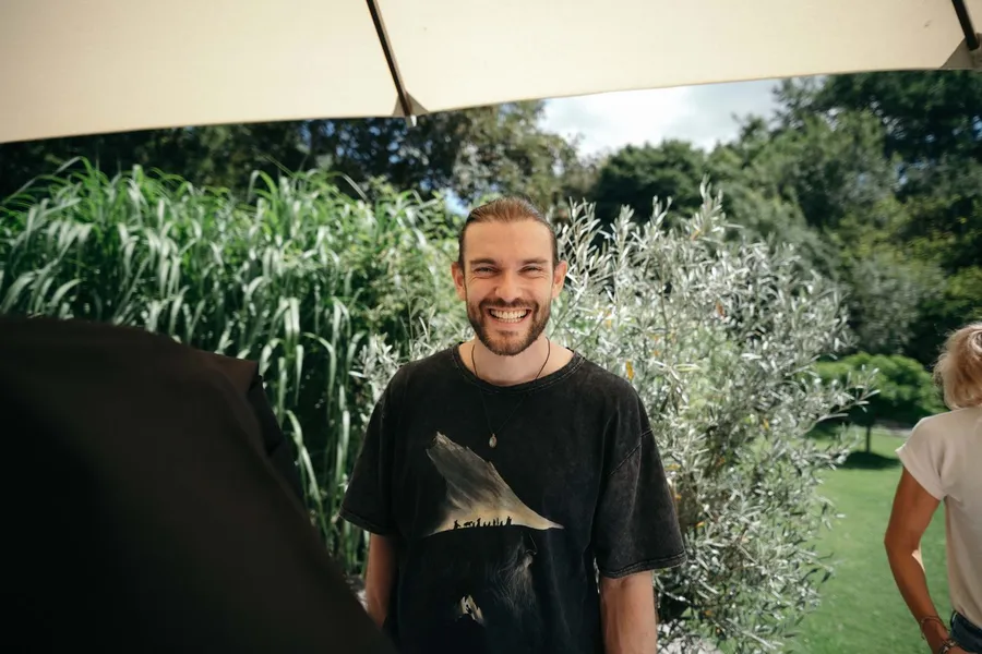 Man laughing under a parasol in a garden, backstage on set, flash by Kilian Amrehn