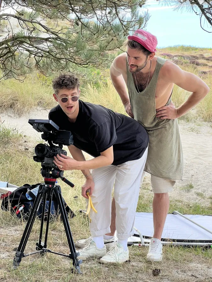 Two men looking at the monitor of a camera on a tripod in the dunes, flash by Kilian Amrehn