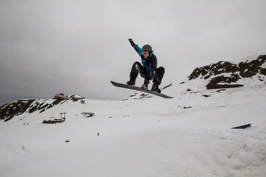 Snowboarder mid-jump over a snowy slope under a grey sky, flash by Kilian Amrehn