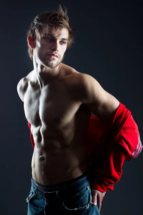 Studio portrait of a young shirtless man with a red jacket, flash by Kilian Amrehn