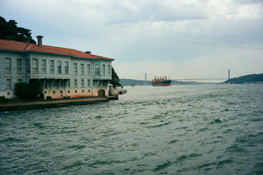 Bosphorus with an old waterfront house, freighter and bridge under clouds, Istanbul, flash by Kilian Amrehn