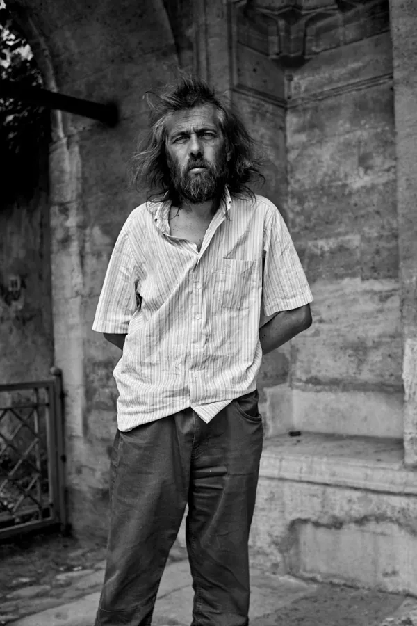 Black and white: man with wild hair and beard in a shirt by a stone arch, Istanbul, flash by Kilian Amrehn