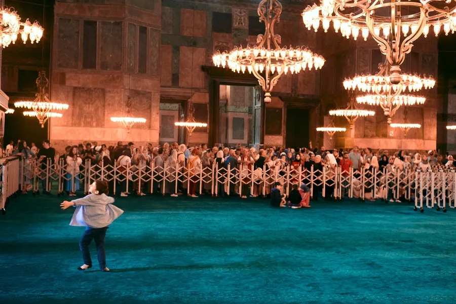 Child spinning on a turquoise carpet under the chandeliers of Hagia Sophia, Istanbul, flash by Kilian Amrehn