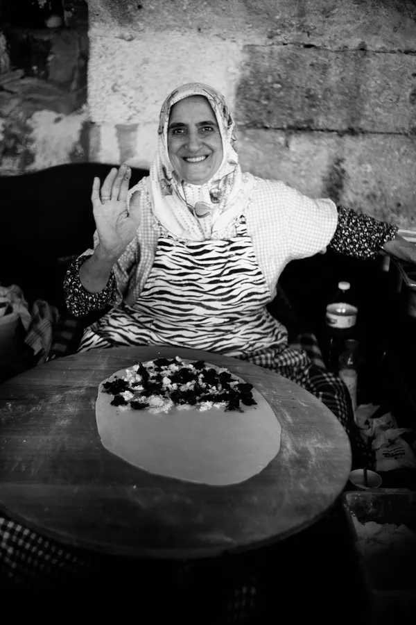 Black and white: woman in a headscarf waving and laughing while making gözleme, Istanbul, flash by Kilian Amrehn