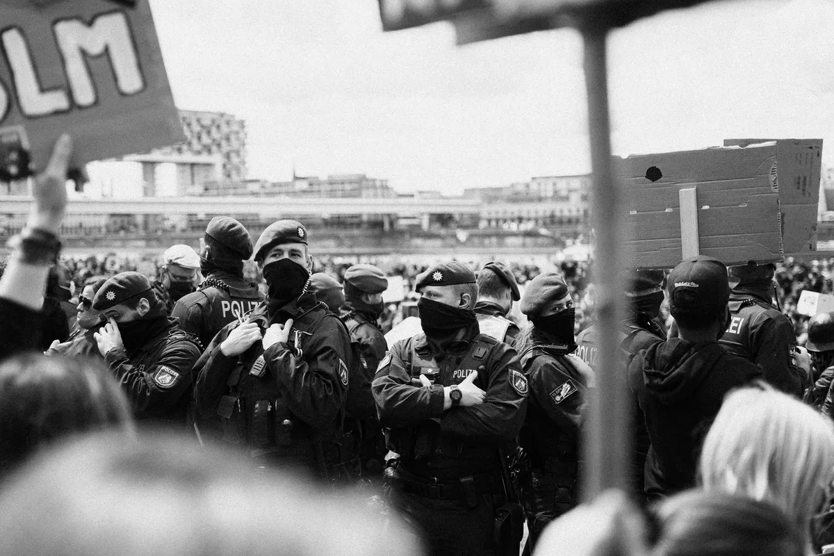 Polizeibeamte mit Mundschutz zwischen Demonstrierenden und Protestschildern, schwarzweiß, Black Lives Matter Köln 2020, Reportage von Kilian Amrehn