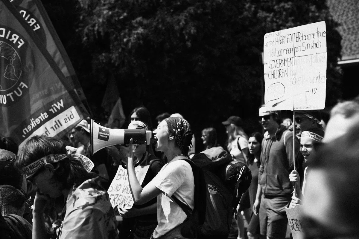 Junge Frau ruft durch ein Megafon, Fridays-for-Future-Fahne und Protestschilder, schwarzweiß, Fridays for Future Garzweiler 2019, Reportage von Kilian Amrehn