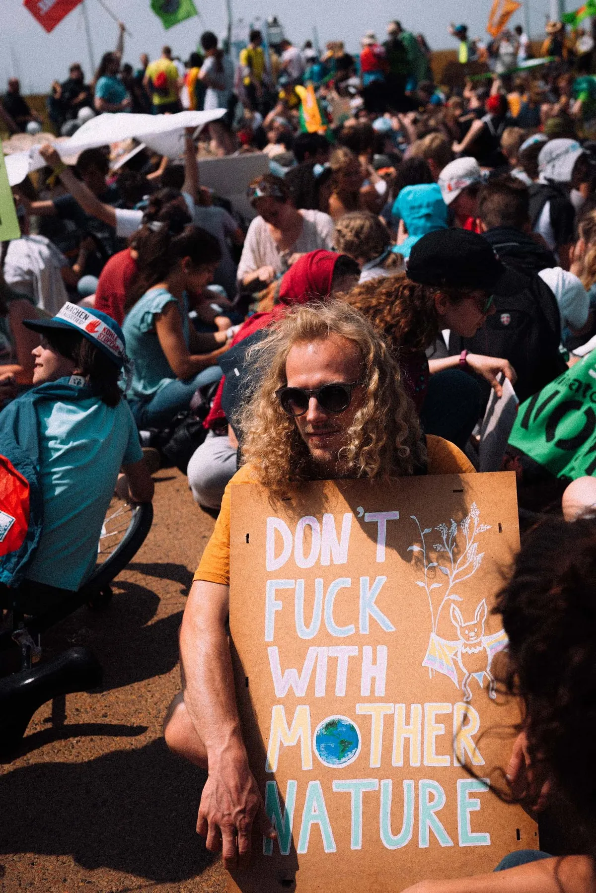 Mann mit Locken und Sonnenbrille hält Schild Don't Fuck With Mother Nature in sitzender Menge, Fridays for Future Garzweiler 2019, Reportage von Kilian Amrehn