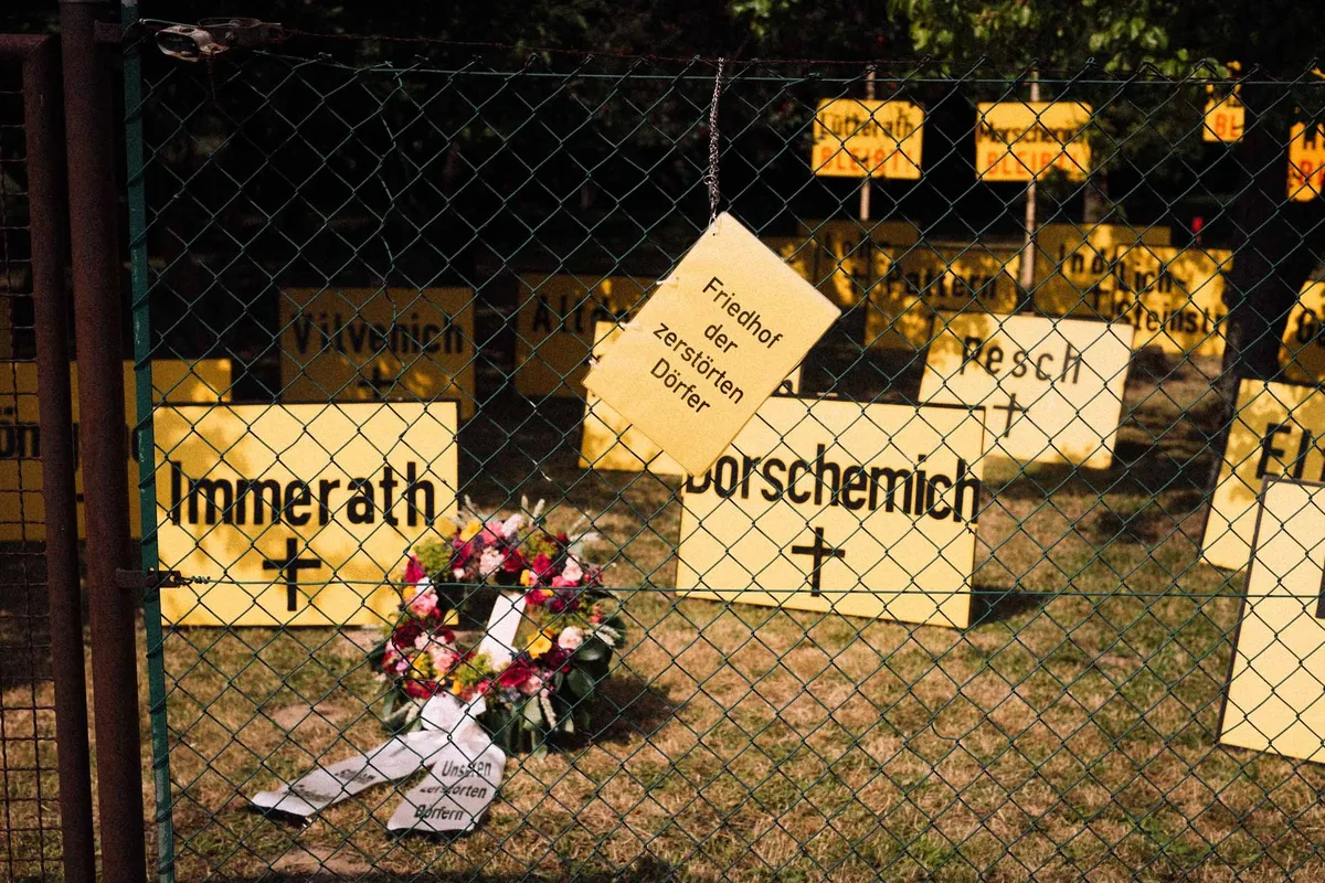 Ortsschilder abgebaggerter Dörfer mit Kreuzen und Kranz hinter Maschendrahtzaun, Friedhof der zerstörten Dörfer, Garzweiler 2019, Reportage von Kilian Amrehn