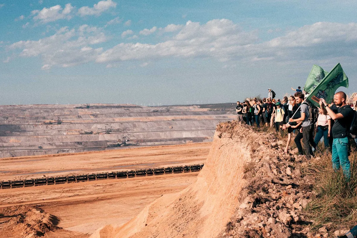 Demonstrierende mit grünen Fahnen auf einem Sandgrat über dem Tagebau, blauer Himmel, Hambacher Forst 2018, Reportage von Kilian Amrehn