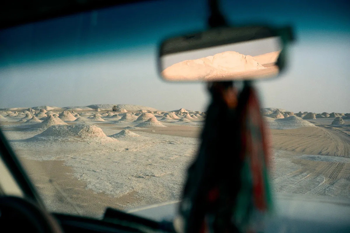 Blick durch die Windschutzscheibe auf weiße Felsformationen in der Wüste, Rückspiegel und Quaste unscharf, Ägypten 2023, Reportage von Kilian Amrehn