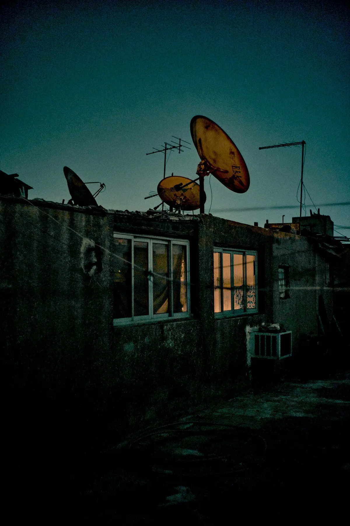 Hausdach mit rostigen Satellitenschüsseln und beleuchtetem Fenster in der Dämmerung, blaugrüne Töne, Kairo 2023, Reportage von Kilian Amrehn