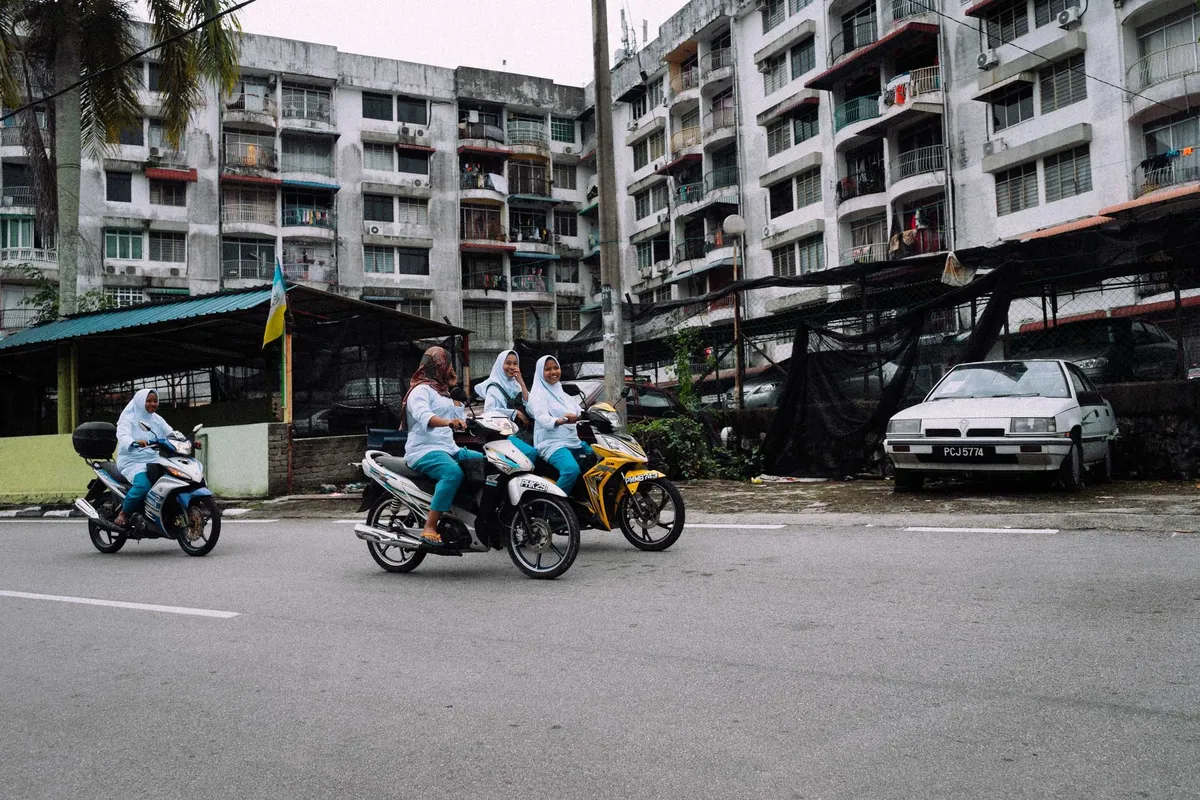 Frauen mit Kopftuch auf Motorrollern vor hohen Wohnblocks mit Balkonen, bewölkter Himmel, Malaysia 2017, Reportage von Kilian Amrehn