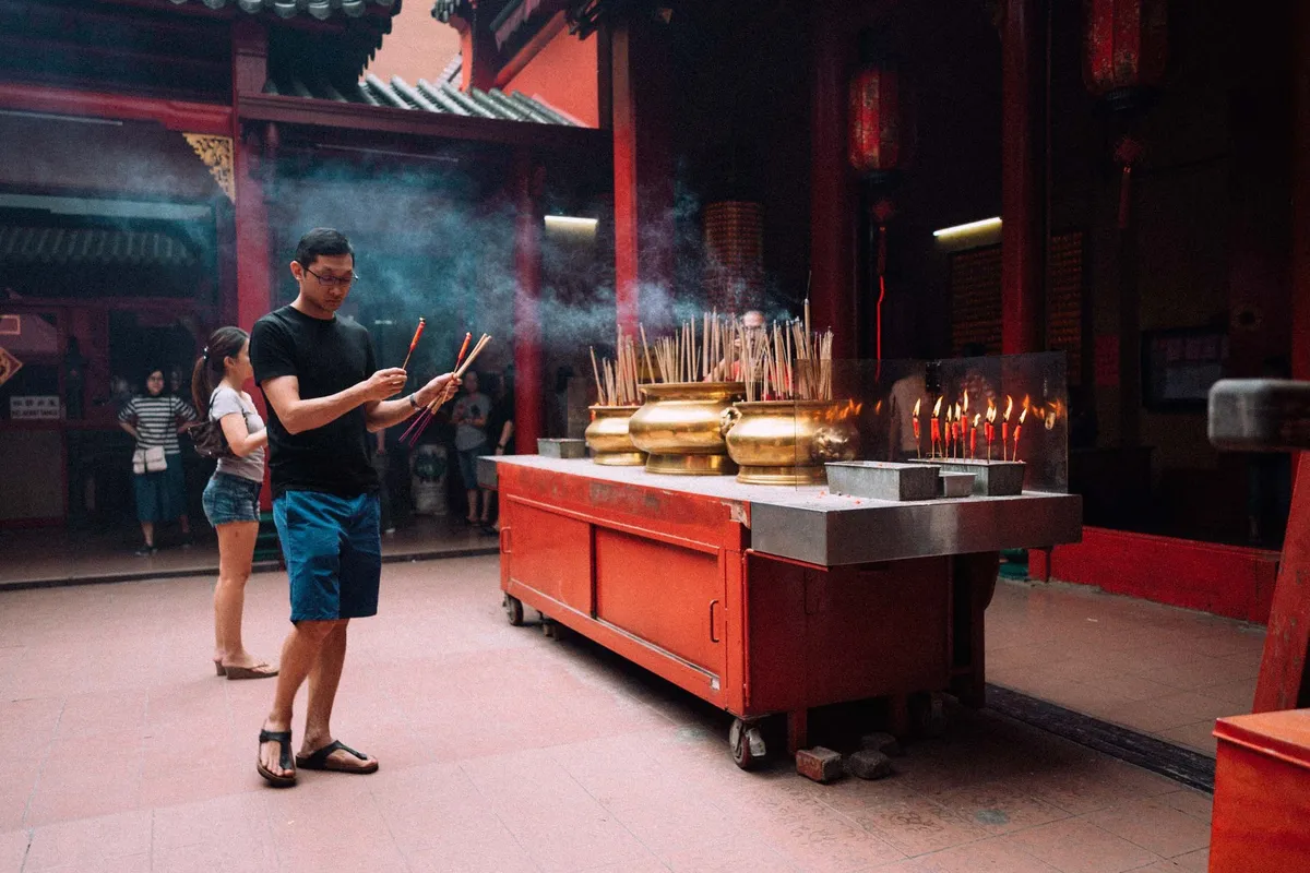 Mann mit Räucherstäbchen vor goldenen Gefäßen in einem roten Tempel, Rauch in der Luft, Malaysia 2017, Reportage von Kilian Amrehn
