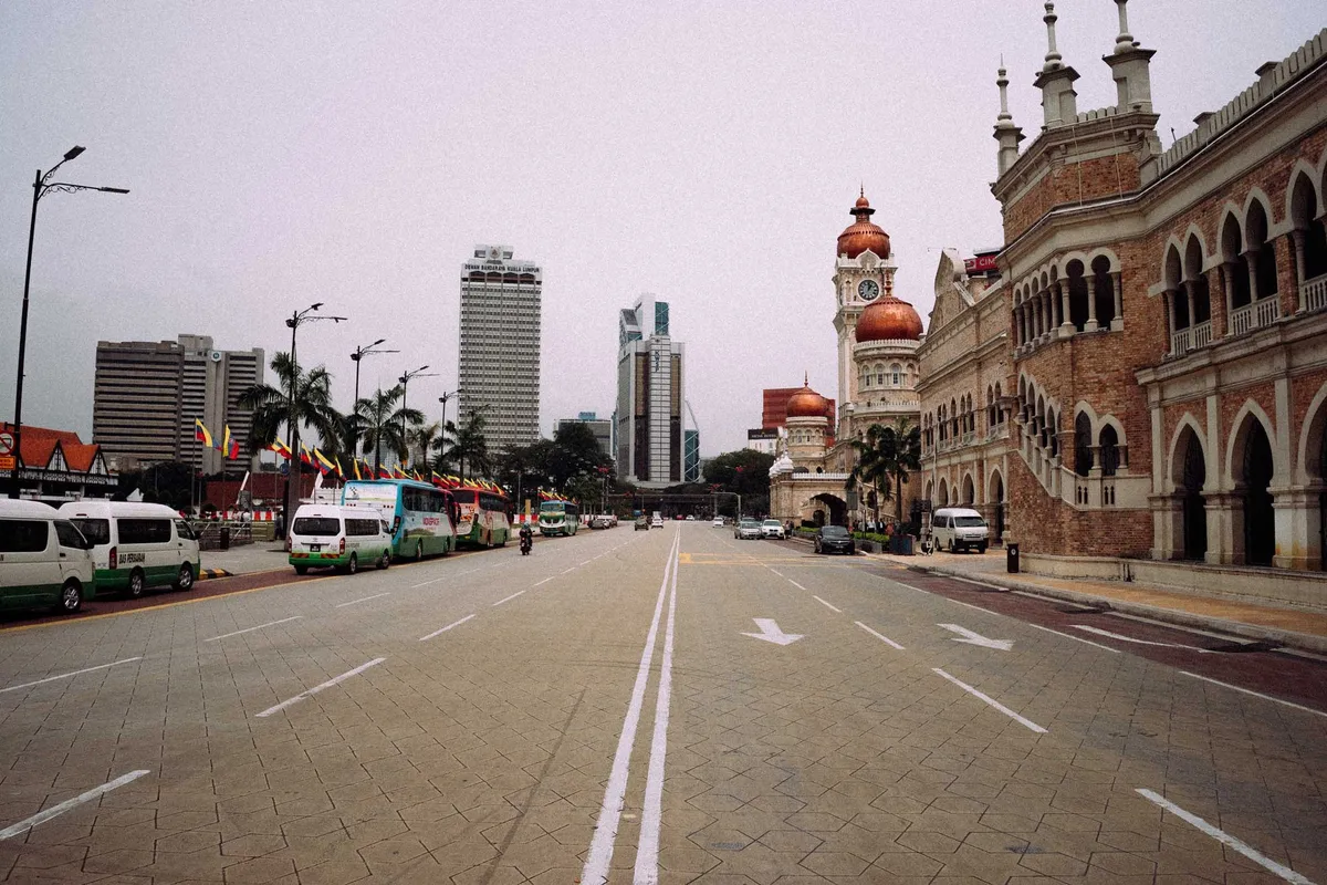 Breite leere Straße vor Kolonialbau mit Kupferkuppeln und Uhrturm, Hochhäuser im Hintergrund, Malaysia 2017, Reportage von Kilian Amrehn