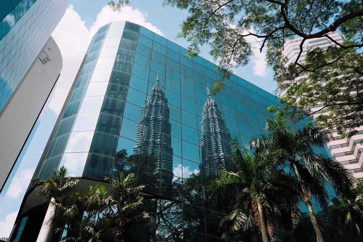 Glasfassade spiegelt zwei Zwillingstürme, Palmen und Äste vor blauem Himmel, Untersicht, Malaysia 2017, Reportage von Kilian Amrehn