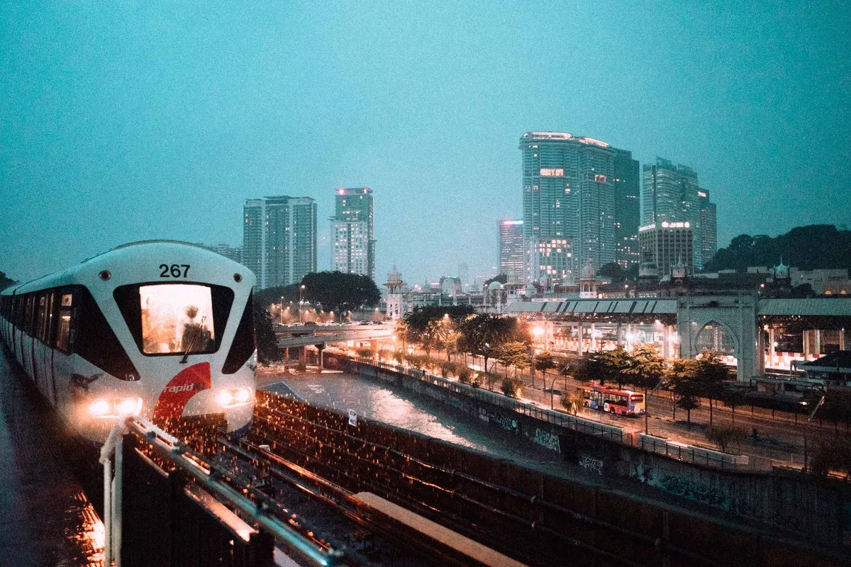 Hochbahn mit leuchtenden Scheinwerfern fährt in der Dämmerung auf die Skyline zu, türkiser Himmel, Malaysia 2017, Reportage von Kilian Amrehn
