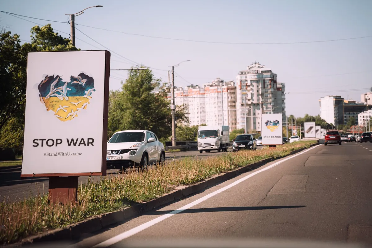 Plakat Stop War mit blau-gelbem Herz am Straßenrand, Autos und Wohnhochhäuser im Abendlicht, Moldau 2022, Reportage von Kilian Amrehn