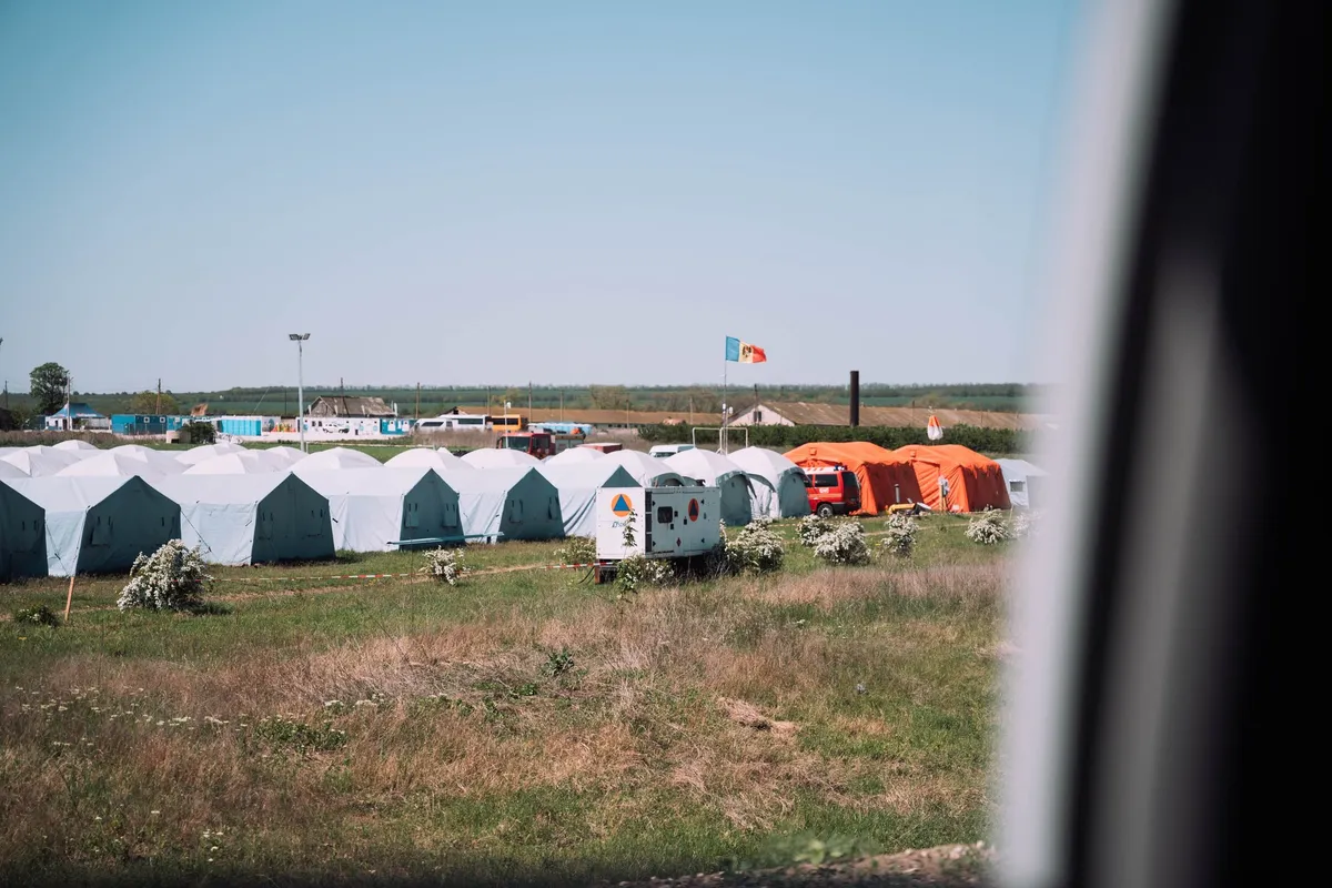Reihen weißer und oranger Zelte auf einer Wiese, Blick aus einem Fahrzeugfenster, blauer Himmel, Flüchtlingsunterkunft in Moldau 2022, Reportage von Kilian Amrehn