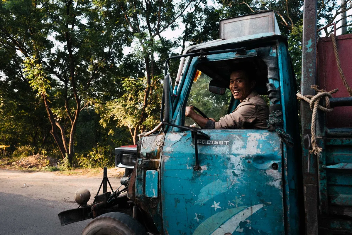 Lachender Fahrer im Führerhaus eines alten türkisblauen Lastwagens, Bäume im Abendlicht, Myanmar 2017, Reportage von Kilian Amrehn