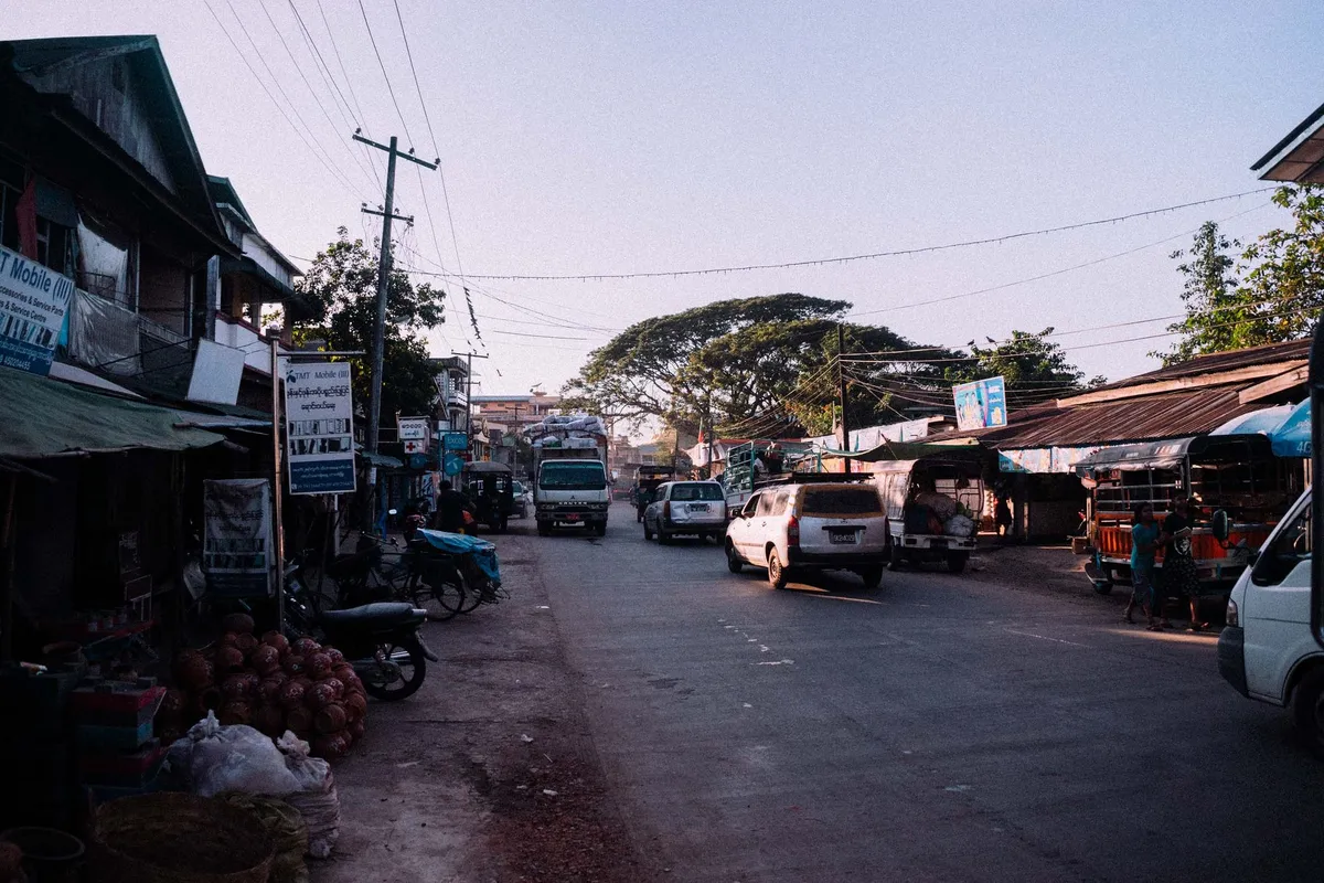 Straße mit Läden, Stromleitungen und Lastwagen im weichen Morgenlicht, Säcke am Straßenrand, Myanmar 2017, Reportage von Kilian Amrehn