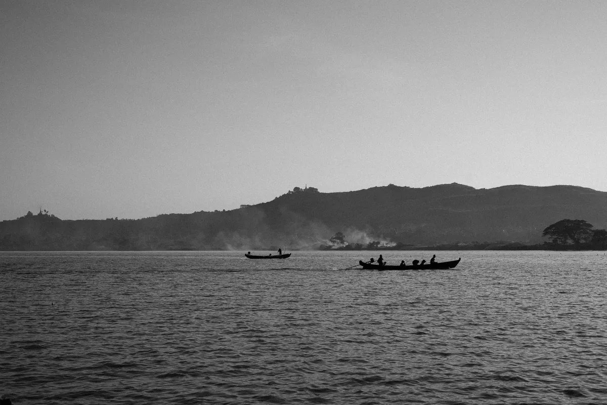Zwei Holzboote mit Menschen auf einem weiten See vor Hügelkette und Dunst, schwarzweiß, Myanmar 2017, Reportage von Kilian Amrehn