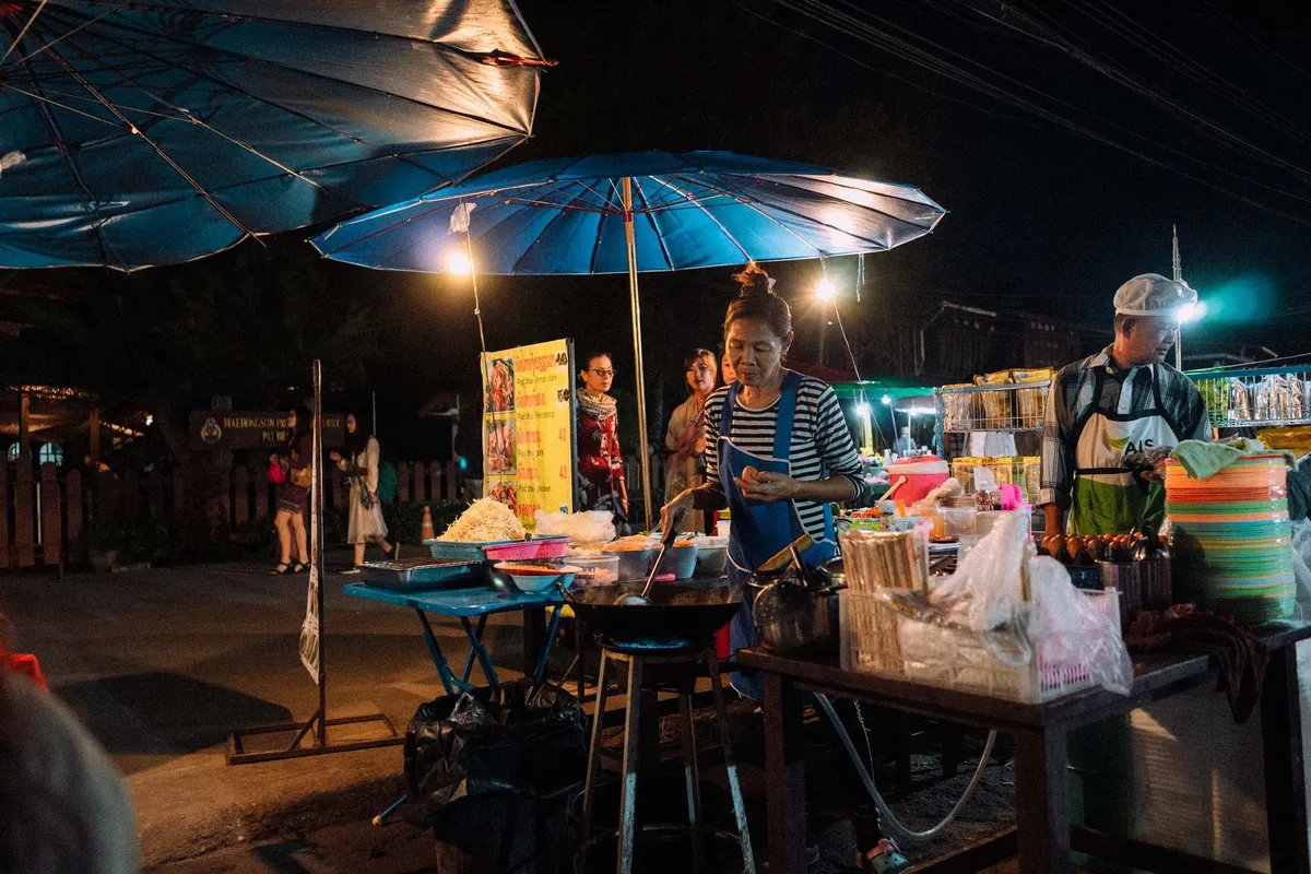 Nachtmarkt mit blauen Schirmen, Frau und Mann kochen an beleuchteten Garküchen, Thailand 2017, Reportage von Kilian Amrehn