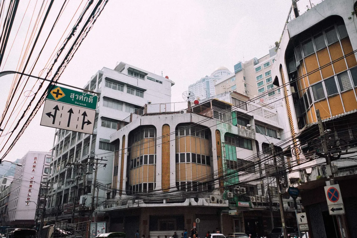 Altes Eckgebäude mit runden Fensterfronten unter einem Gewirr aus Stromkabeln, Straßenschilder, Thailand 2017, Reportage von Kilian Amrehn