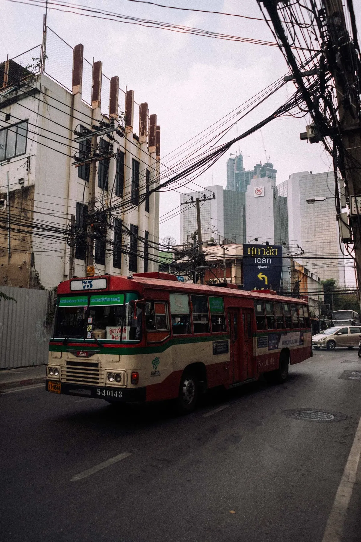 Rot-weißer Stadtbus unter dichten Stromleitungen, Hochhäuser im Hintergrund, Thailand 2017, Reportage von Kilian Amrehn