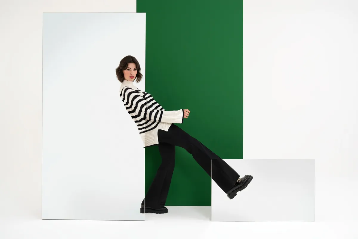AppelrathCüpper, model in a black and white striped sweater kicking one leg before a green panel and mirrors, campaign 2022, photographed by Kilian Amrehn