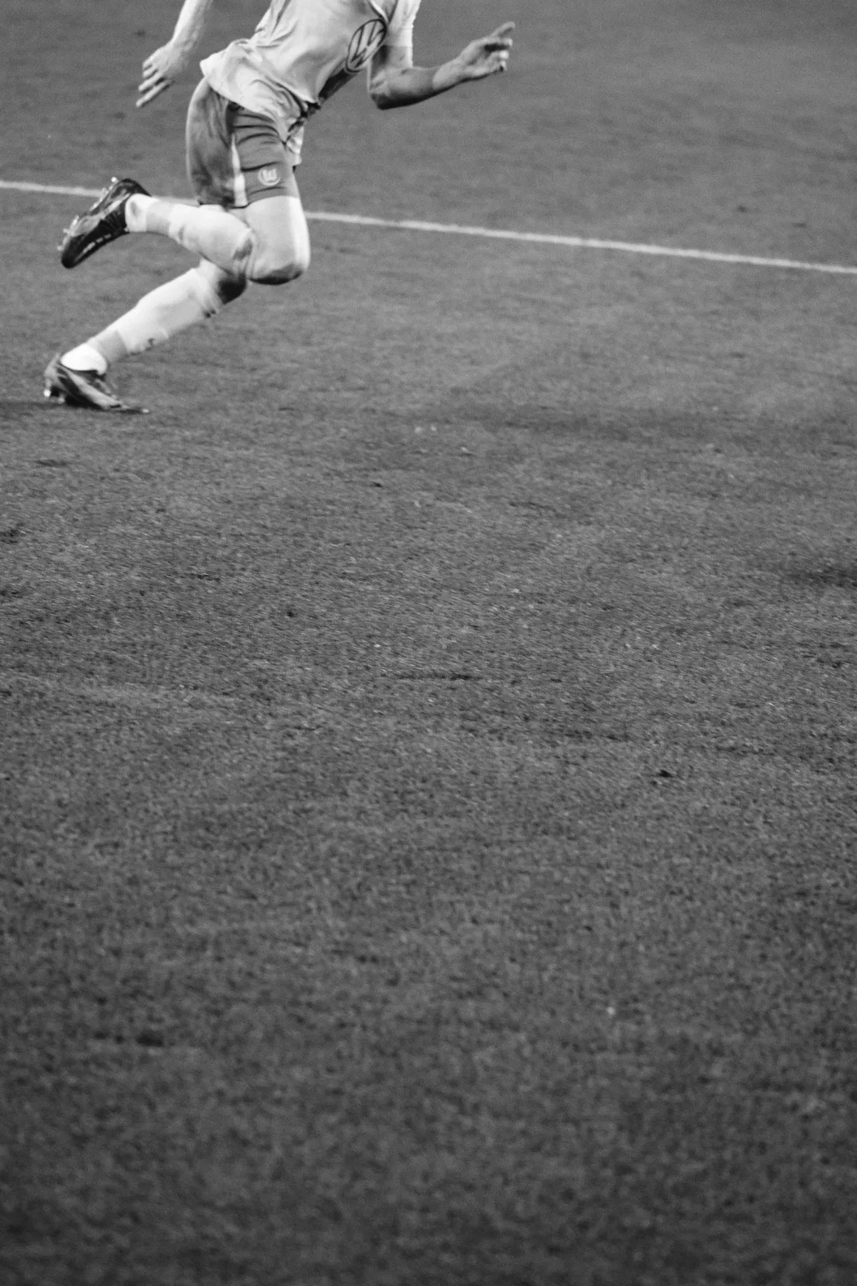 Bundesliga, legs of a running player at the top edge above an expanse of empty grass, minimalist black and white, sports photography, photographed by Kilian Amrehn