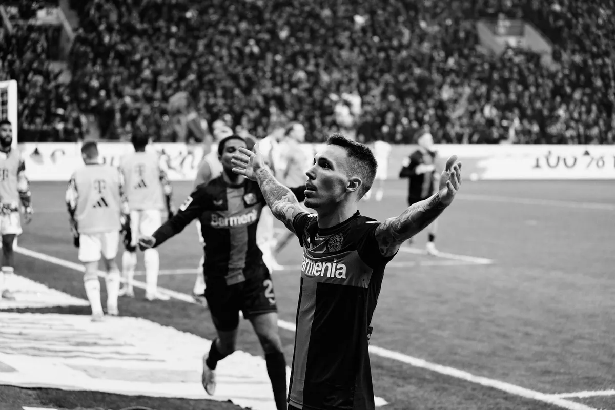 Bundesliga, player with tattooed arms spreading his arms in celebration in front of the stands, black and white, sports photography, photographed by Kilian Amrehn