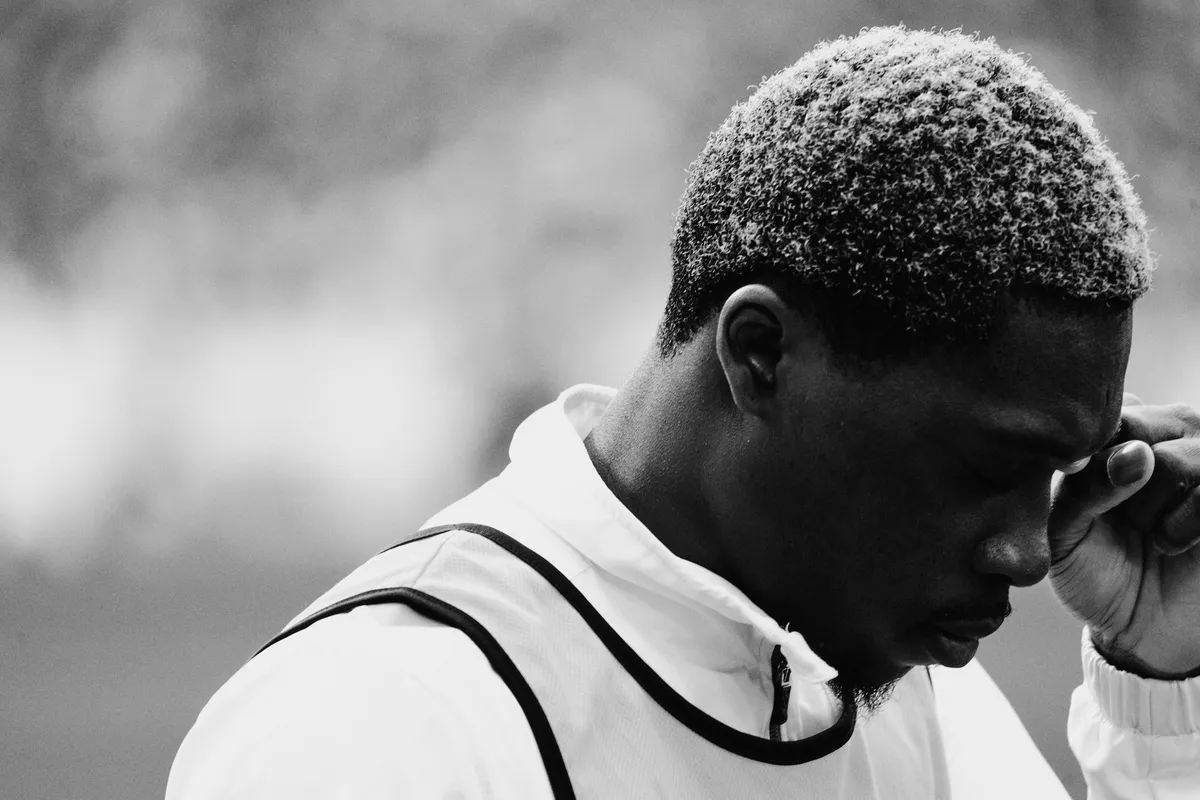 Bundesliga, player in a training bib lowering his head in thought, hand at temple, black and white close-up, sports photography, photographed by Kilian Amrehn