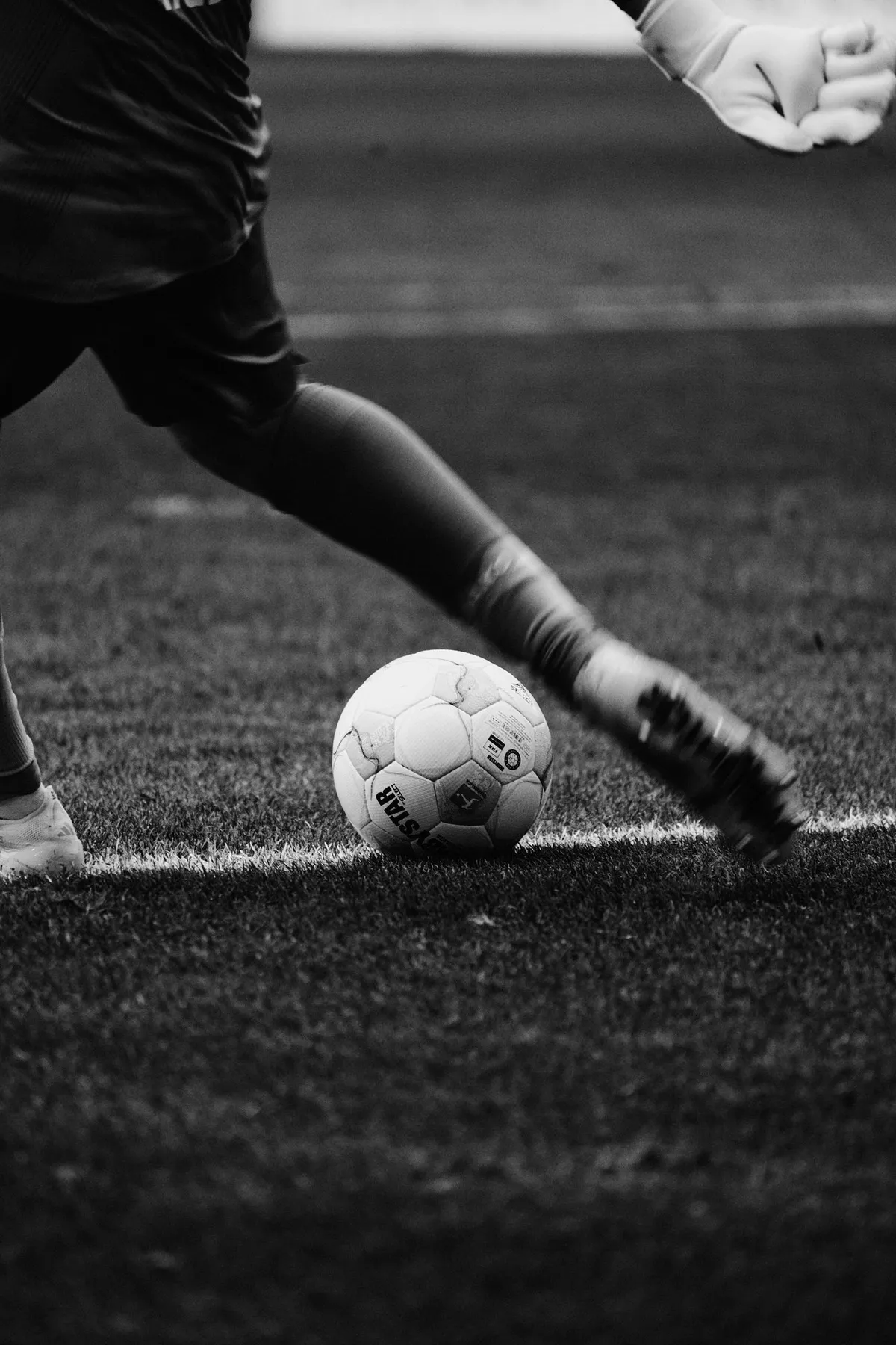 Bundesliga, detail of a player striking the ball, boot and ball on the grass, black and white, sports photography, photographed by Kilian Amrehn
