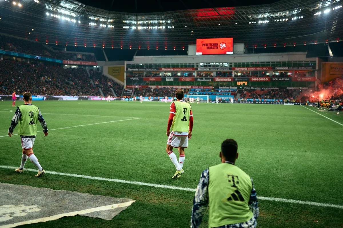 Bundesliga, substitutes in green bibs warming up at the touchline, floodlit stadium with flares in the stand, sports photography, photographed by Kilian Amrehn