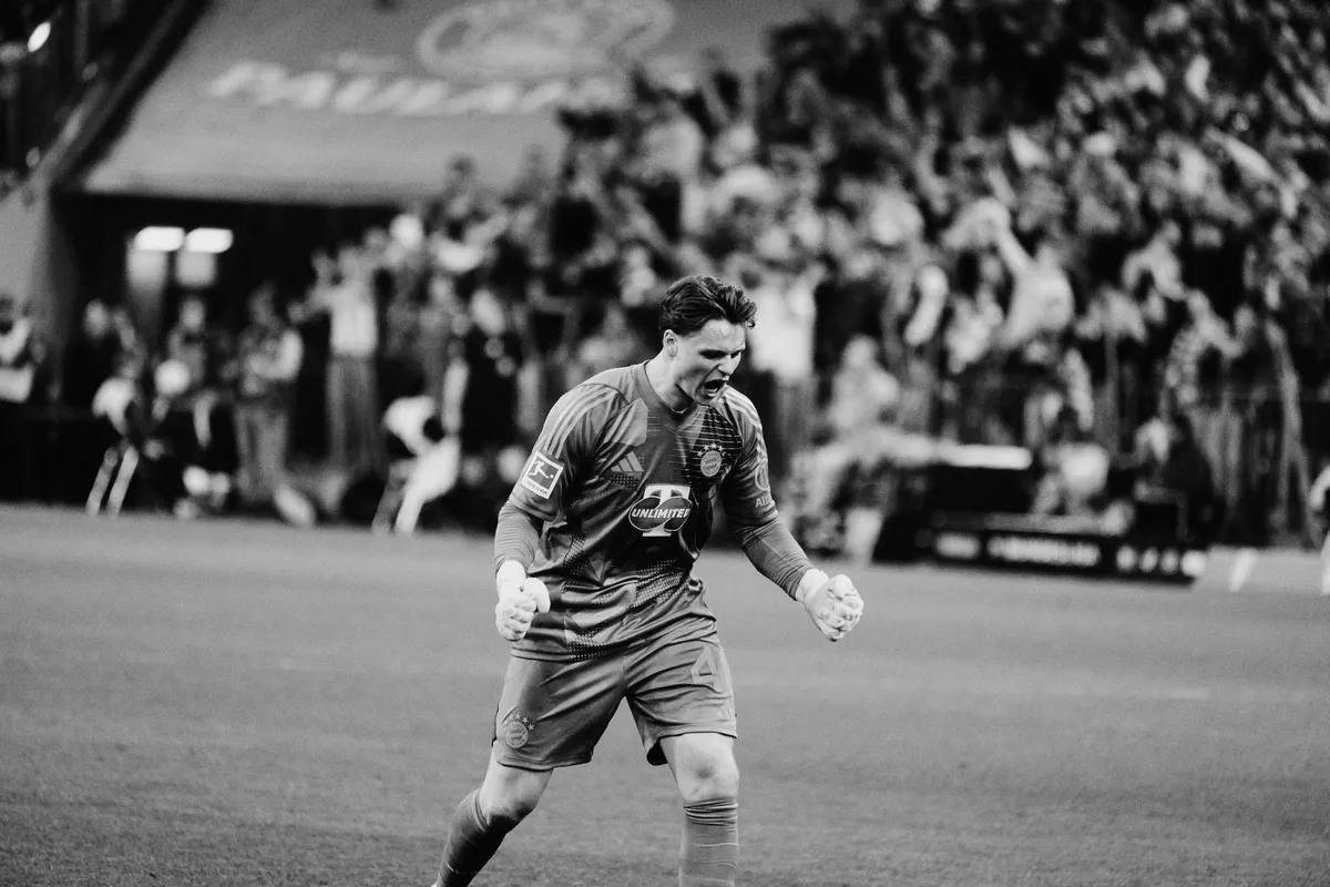 Bundesliga, goalkeeper clenching his fists in celebration in front of the fan stand, black and white, sports photography, photographed by Kilian Amrehn