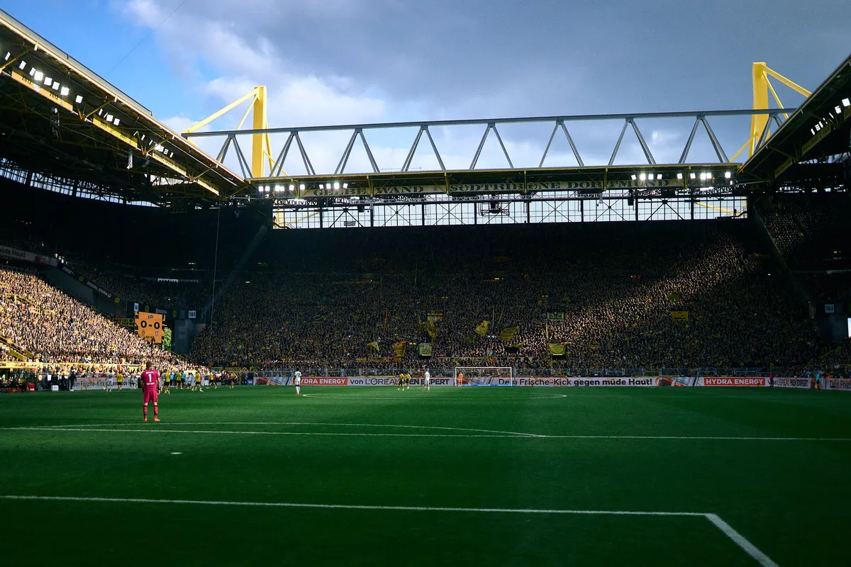 Bundesliga, stadium with yellow roof pylons and sunlit stands, goalkeeper in the box, blue sky, sports photography, photographed by Kilian Amrehn