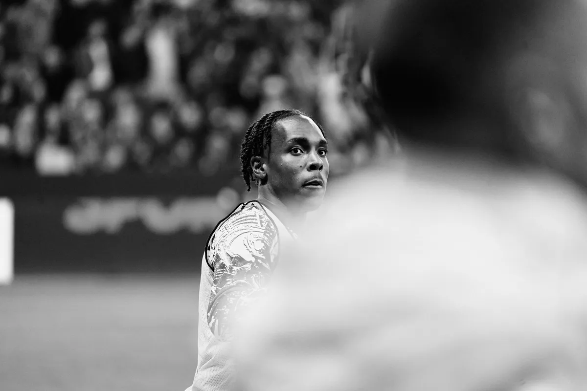 Bundesliga, player with braided hair looking over his shoulder, blurred figure in the foreground, black and white, sports photography, photographed by Kilian Amrehn