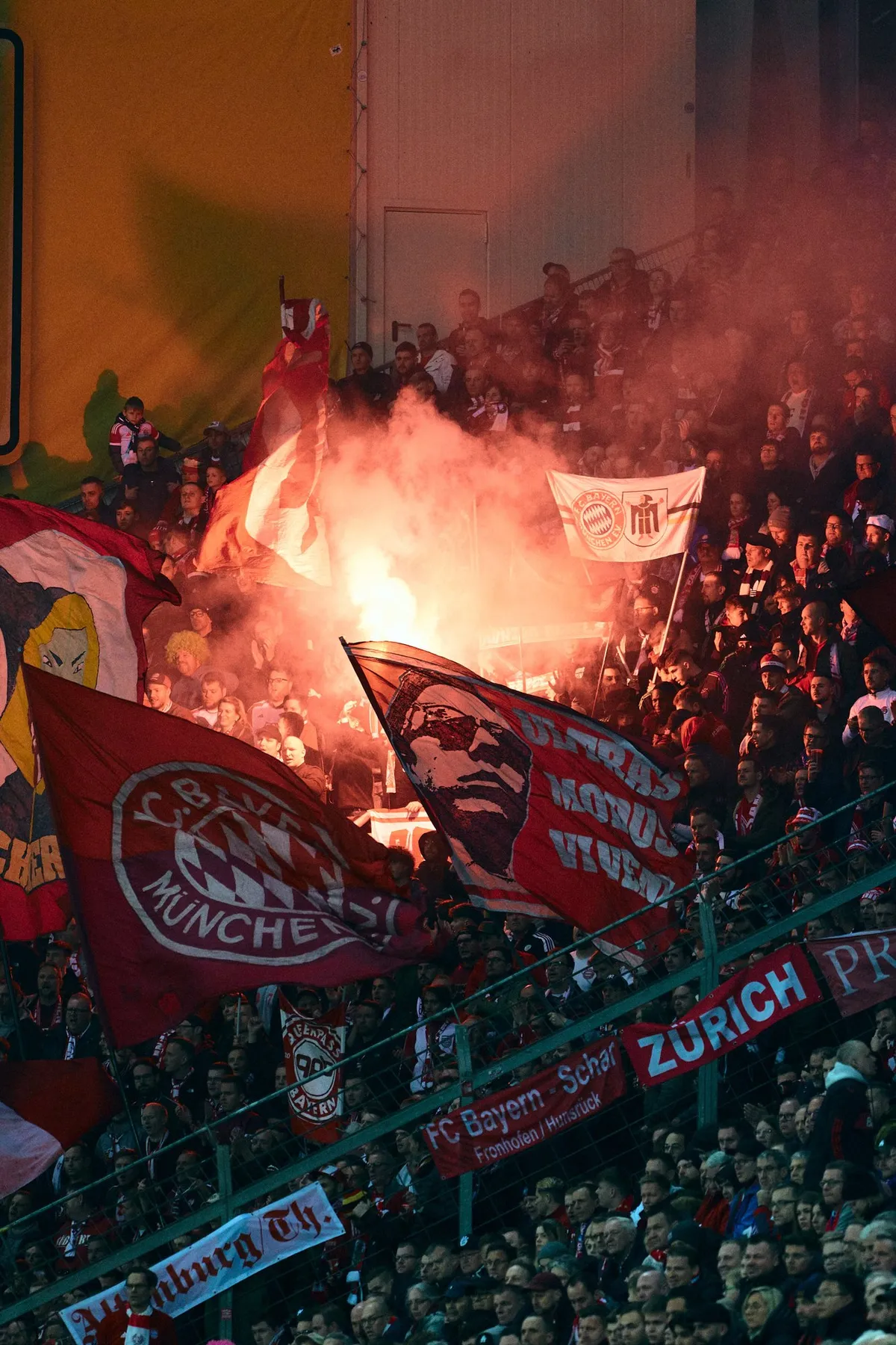 Bundesliga, fan stand with FC Bayern flags and burning flares in red smoke, sports photography, photographed by Kilian Amrehn