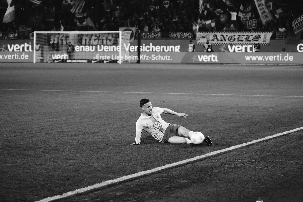 Bundesliga, player sliding into the ball at the touchline in front of ad boards and fan block, black and white, sports photography, photographed by Kilian Amrehn